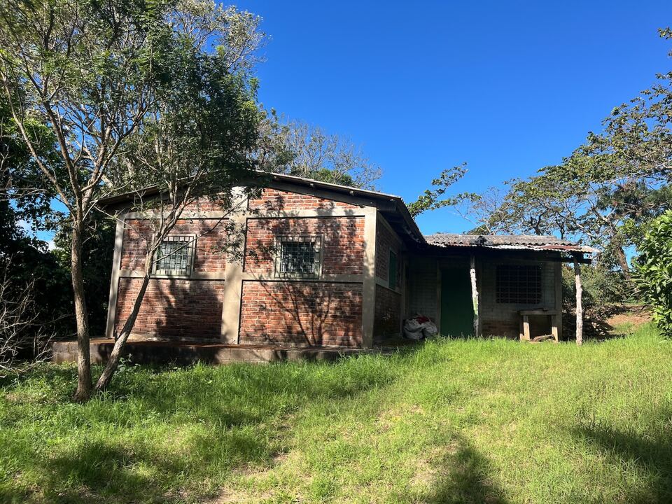 Una casa de finca de ladrillo en un claro con pasto, entre árboles.